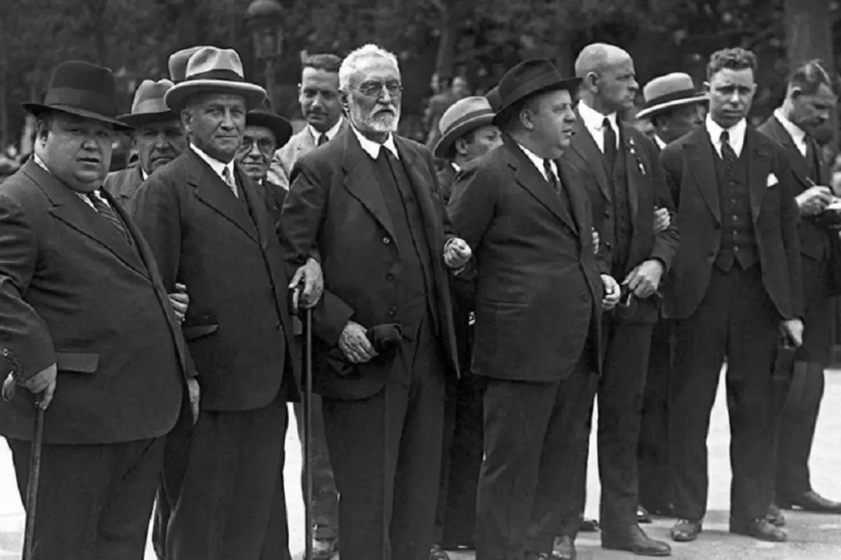 Grupo de hombres con traje y sombrero tomados del brazo en una calle durante una manifestación histórica en blanco y negro