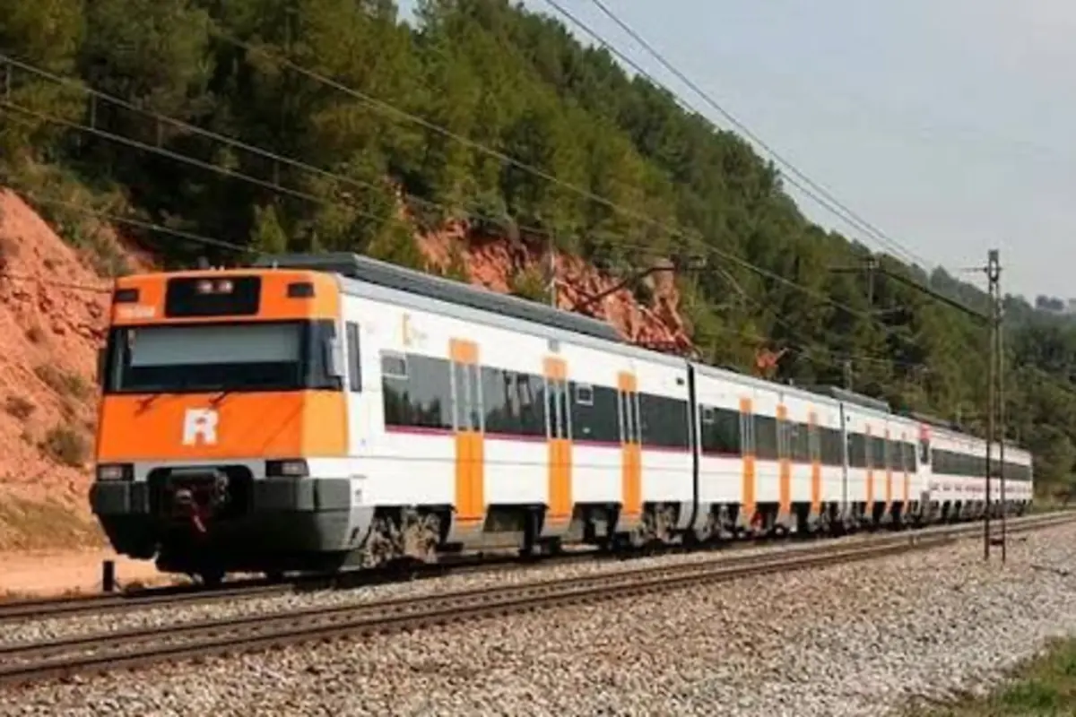 Tren de cercanías blanco y naranja circulando por una vía férrea entre árboles y taludes de tierra Tren de cercanías blanco y naranja circulando por una vía férrea entre árboles y taludes de tierra