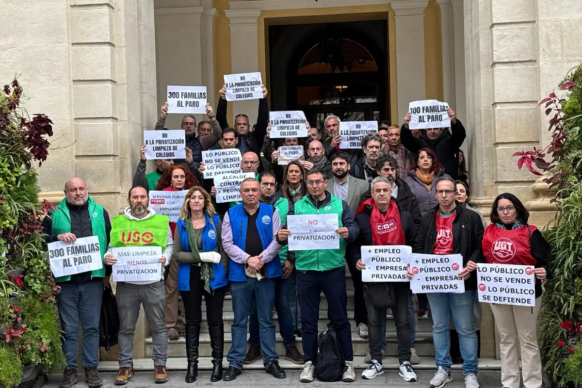 Grupo de trabajadores y representantes sindicales concentrados en la entrada de un edificio histórico sosteniendo pancartas en defensa de los servicios públicos y contra la privatización de la limpieza de colegios