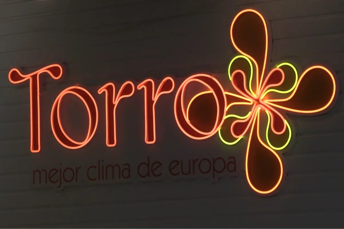 Rótulo luminoso de Torrox con letras rojas y eslogan mejor clima de Europa junto a un diseño decorativo de gotas de colores