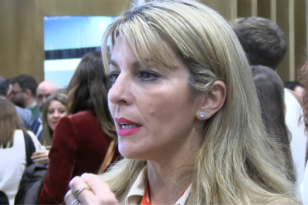 Mujer rubia de perfil en un evento concurrido hablando entre la multitud