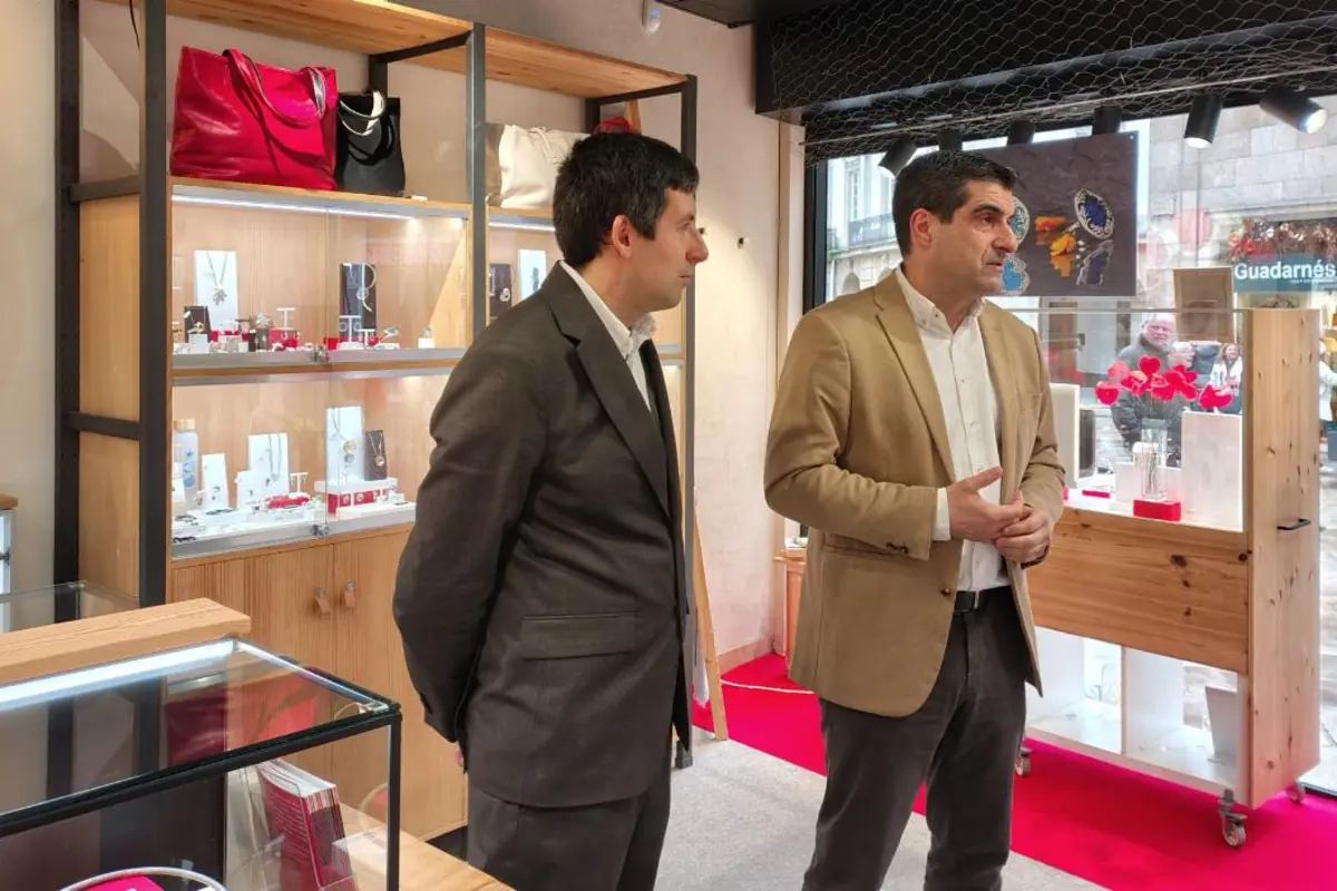 Dos hombres con traje conversan en el interior de una joyería moderna con vitrinas iluminadas y bolsos expuestos en estanterías de madera