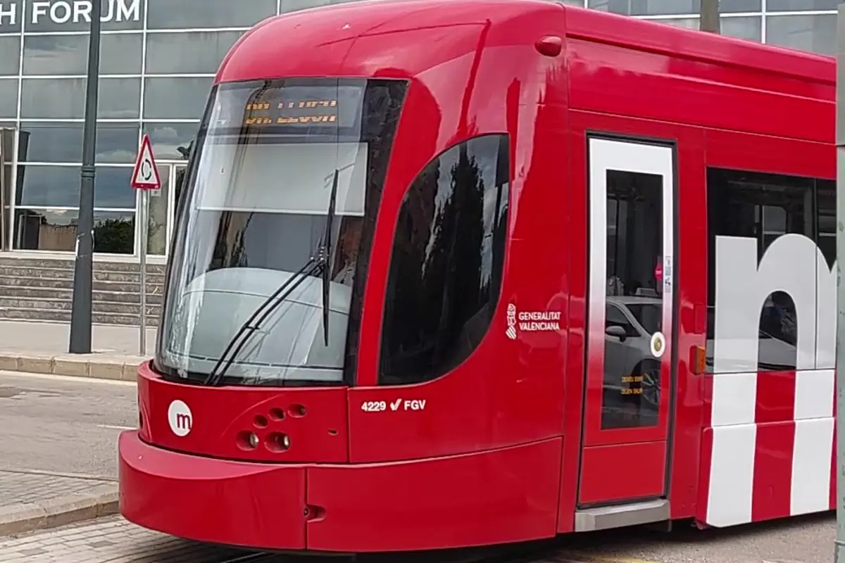 Tranvía rojo moderno de Metrovalencia detenido junto a una acera frente a un edificio acristalado