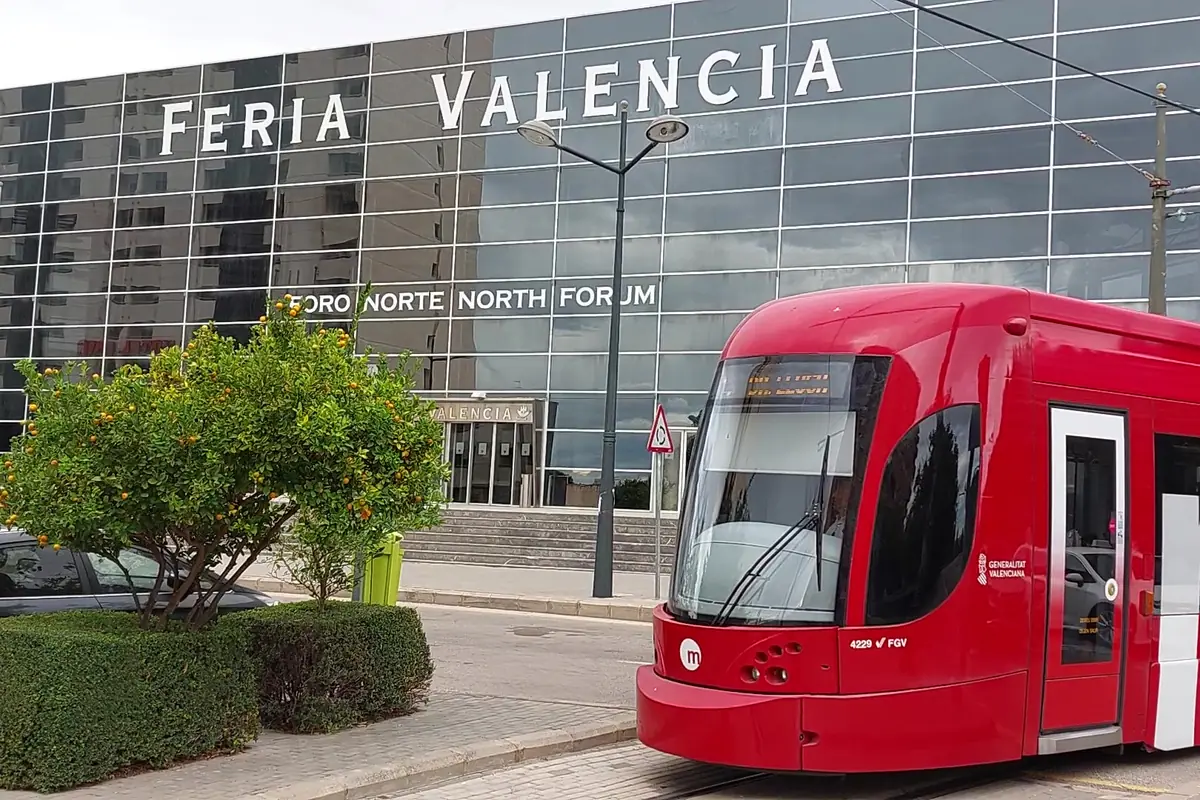 Tranvía rojo de Metrovalencia frente al edificio acristalado de Feria Valencia con naranjos en primer plano