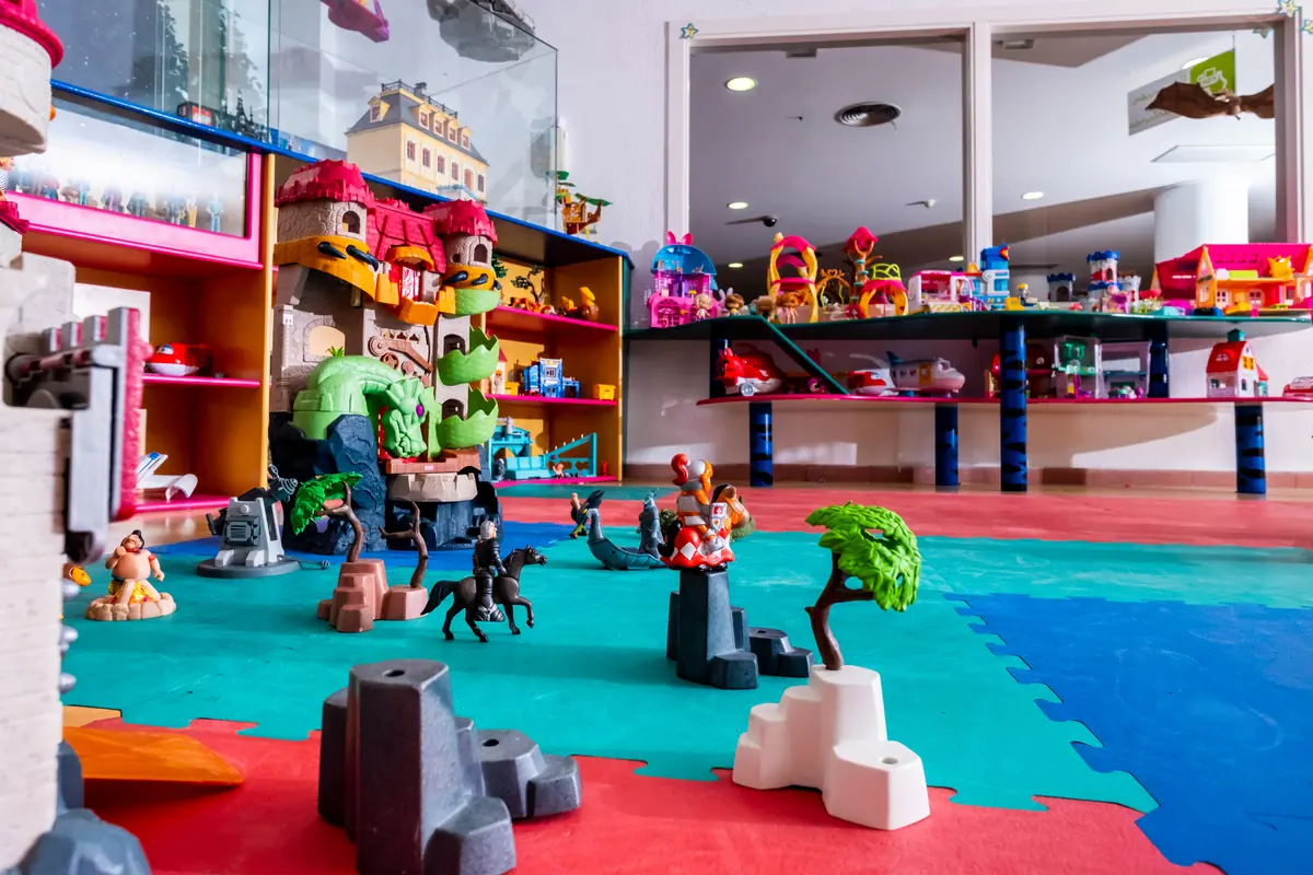 Sala de juegos infantil con alfombra de goma y numerosos juguetes de plástico y figuras de fantasía organizados en estanterías y en el suelo