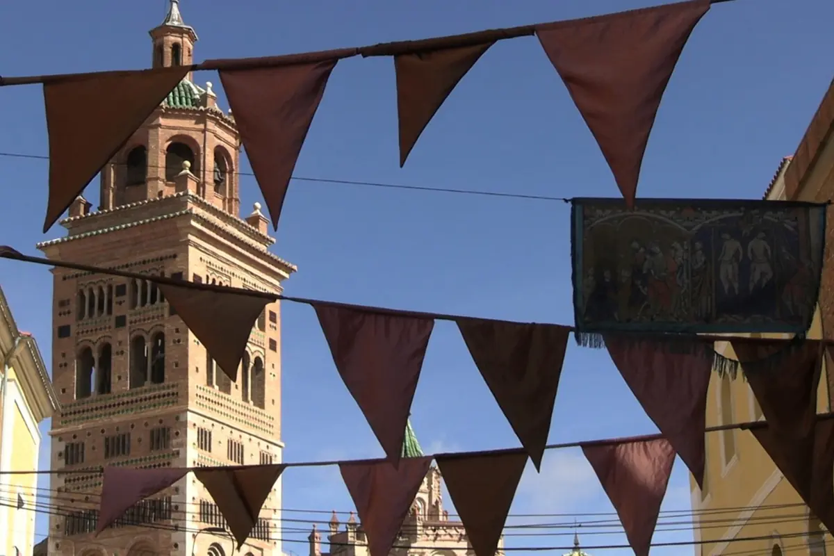 Banderines triangulares colgando en una calle con una torre de ladrillo de estilo histórico al fondo bajo un cielo despejado Banderines triangulares colgando en una calle con una torre de ladrillo de estilo histórico al fondo bajo un cielo despejado