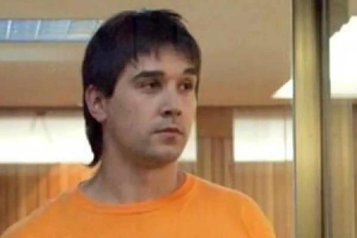 Hombre joven con camiseta naranja mirando hacia un lado en un interior iluminado