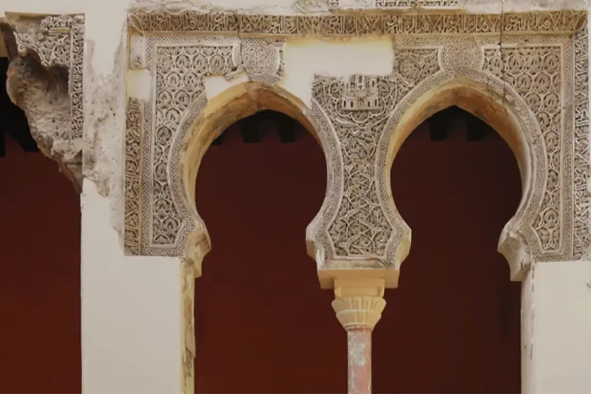 Detalle de arcos de estilo islámico con elaborados relieves geométricos y vegetales en piedra sobre un fondo rojo oscuro