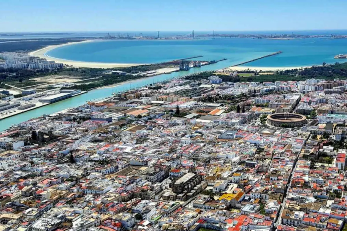 Vista aérea de una ciudad costera con un río que desemboca en el mar, una amplia playa en forma de bahía y una plaza de toros circular entre los edificios Vista aérea de una ciudad costera con un río que desemboca en el mar, una amplia playa en forma de bahía y una plaza de toros circular entre los edificios