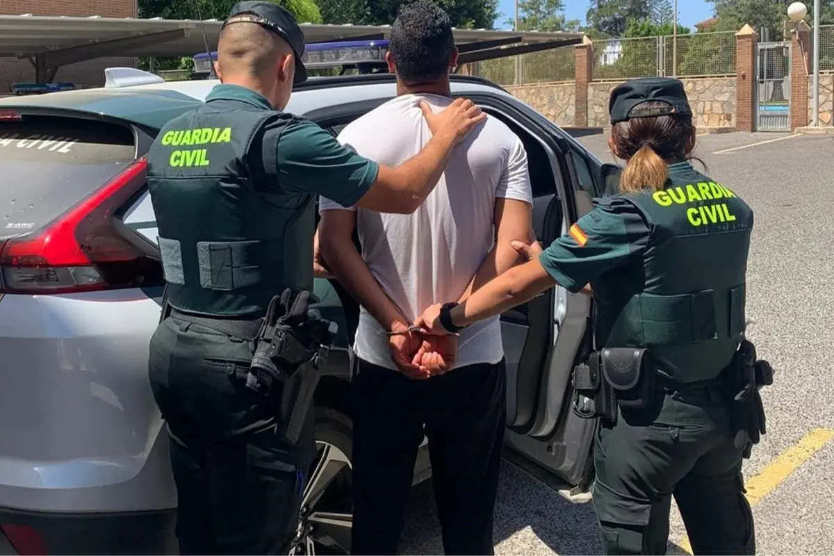 Dos agentes de la Guardia Civil escoltan a un hombre esposado hacia un coche patrulla en un aparcamiento