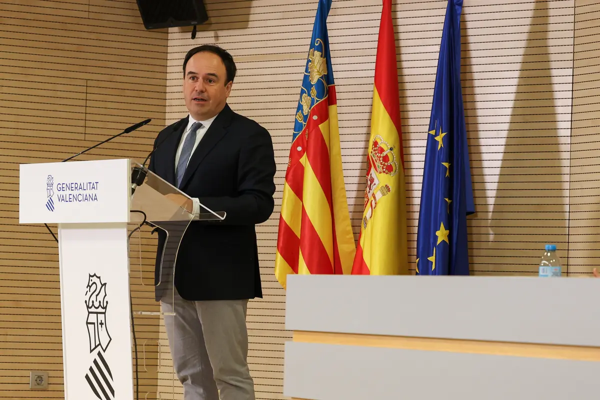 Hombre con traje hablando en un atril de la Generalitat Valenciana junto a las banderas de la Comunidad Valenciana España y la Unión Europea Hombre con traje hablando en un atril de la Generalitat Valenciana junto a las banderas de la Comunidad Valenciana España y la Unión Europea