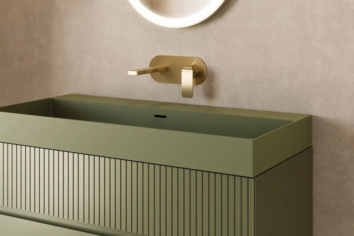 Lavabo moderno verde con mueble estriado y grifería dorada empotrada sobre pared beige