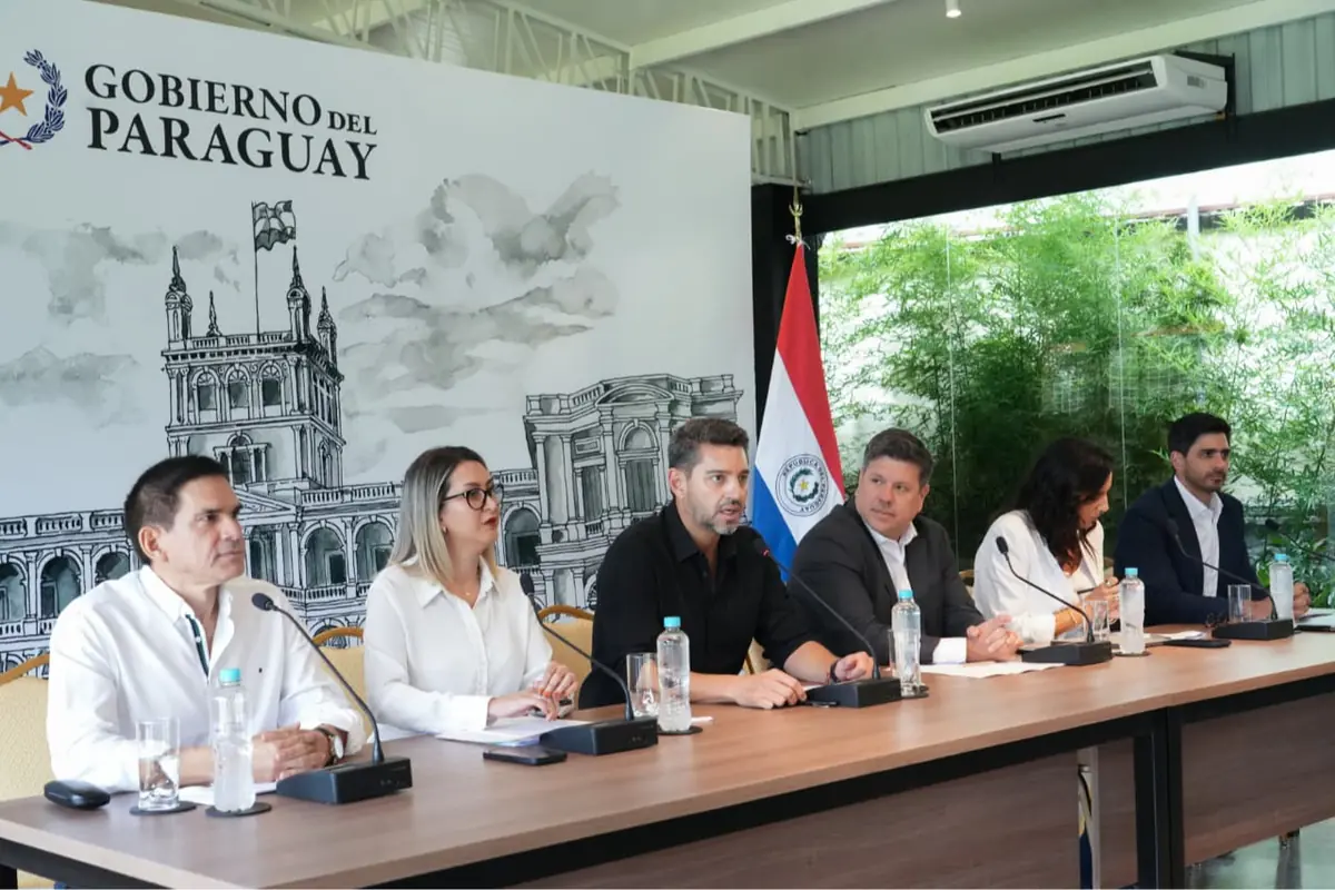 Autoridades del Gobierno de Paraguay sentadas en una mesa larga ofreciendo una conferencia de prensa frente a un panel institucional y la bandera paraguaya Autoridades del Gobierno de Paraguay sentadas en una mesa larga ofreciendo una conferencia de prensa frente a un panel institucional y la bandera paraguaya