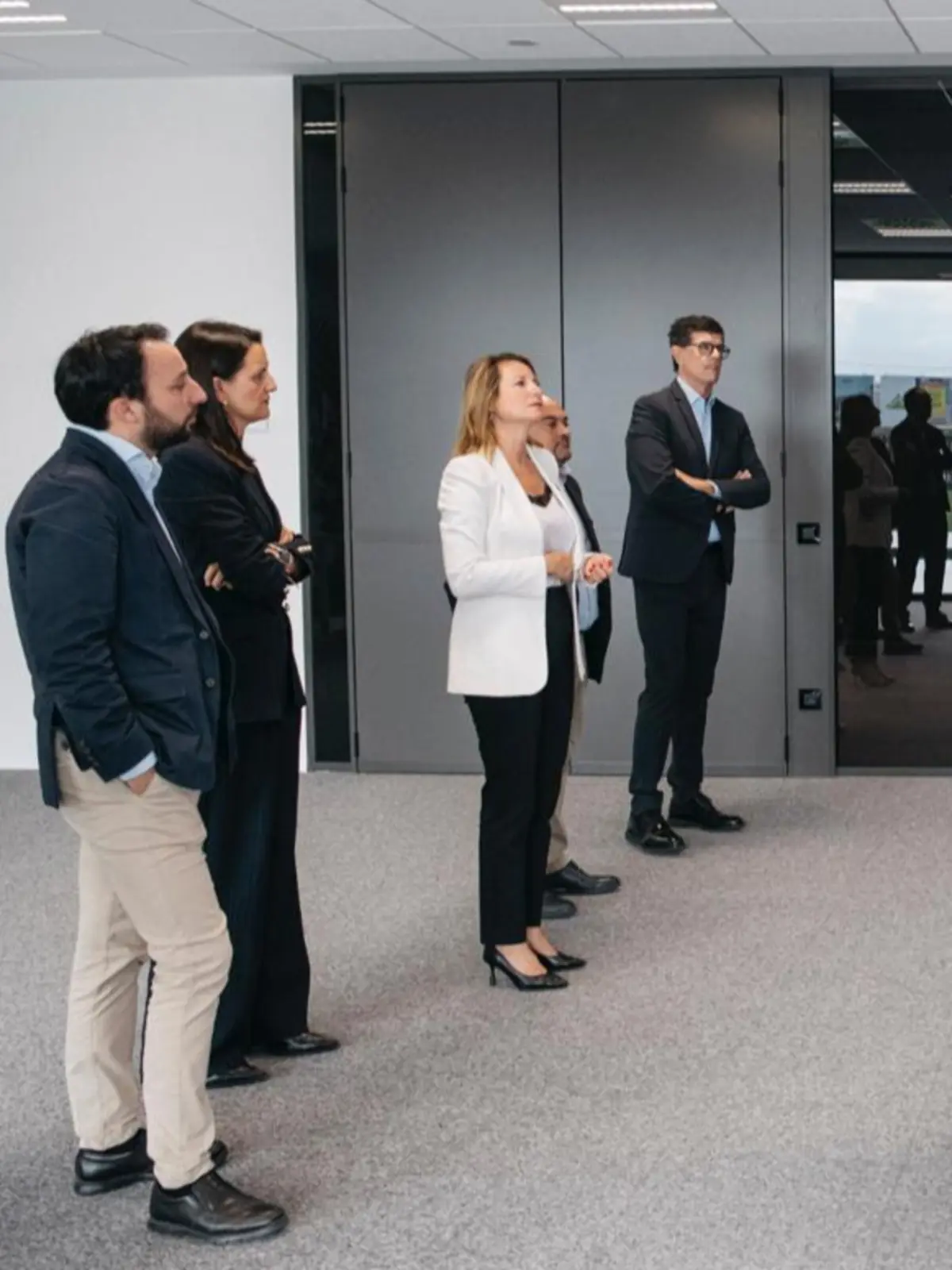 Grupo de personas con ropa de oficina de pie en una sala moderna mirando hacia un punto fuera de cámara
