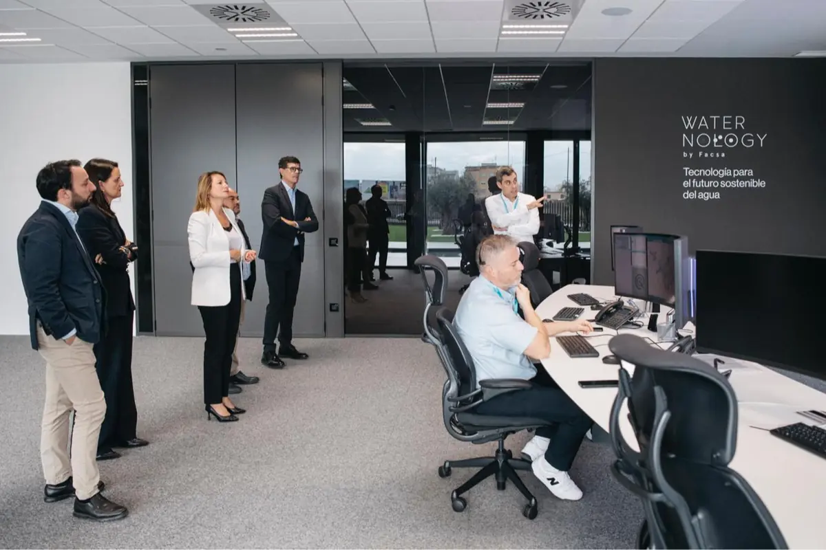 Grupo de profesionales en una sala de control moderna observando a un técnico que trabaja con varios monitores en un centro de tecnología del agua