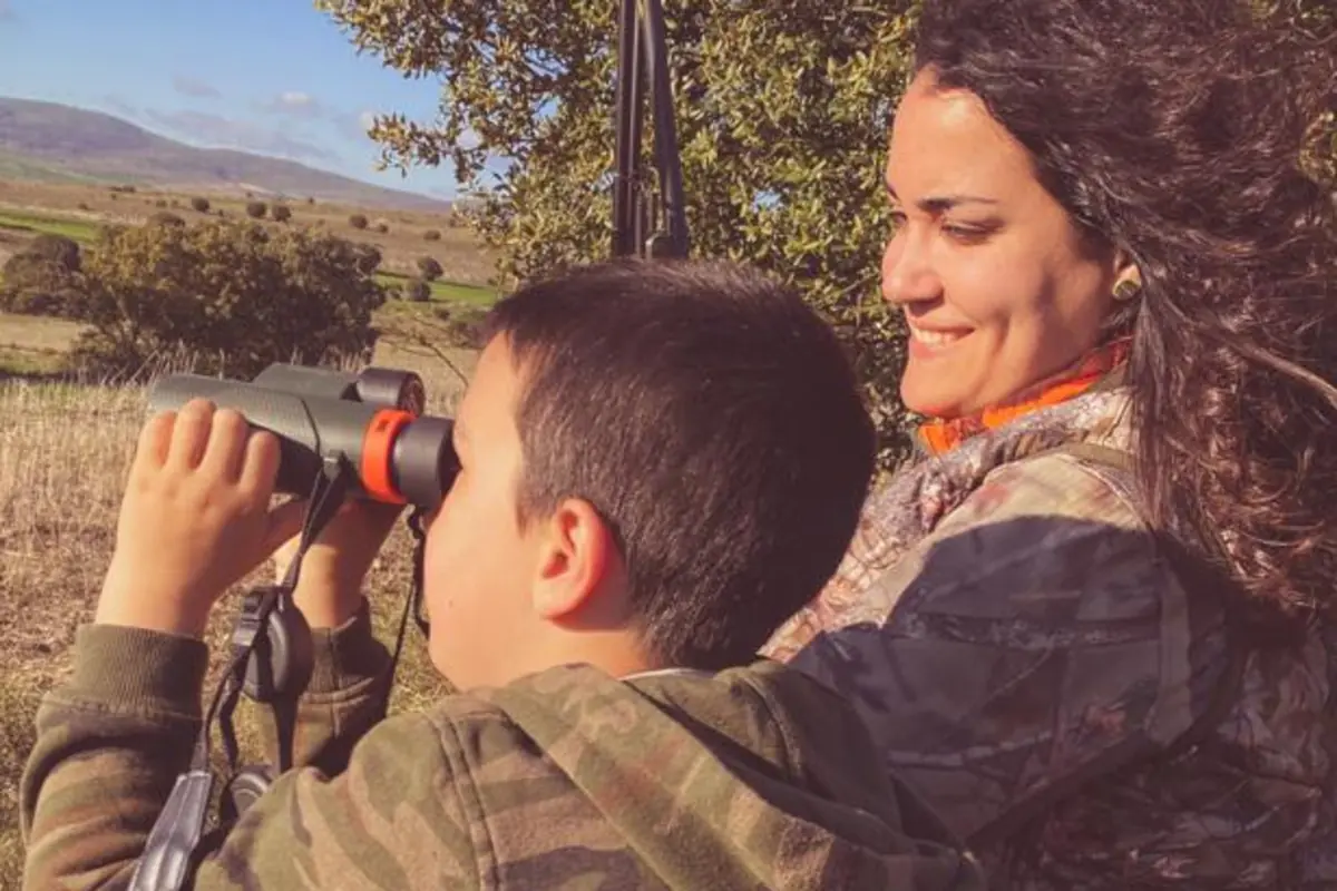 Mujer y niño con ropa de camuflaje observando el paisaje con prismáticos en el campo