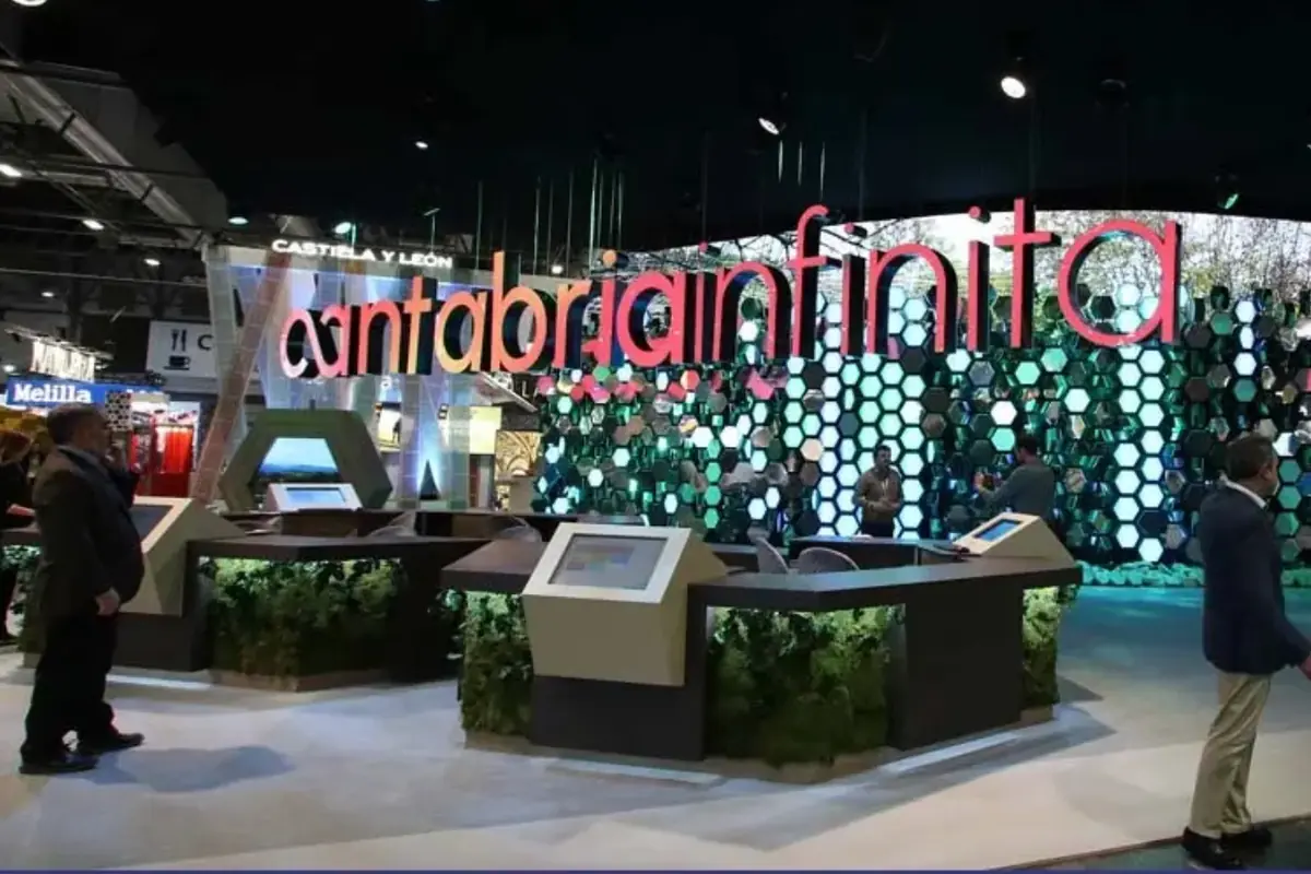 Stand turístico de Cantabria Infinita en una feria con gran letrero luminoso y mostradores interactivos rodeados de decoración verde y paneles hexagonales de colores