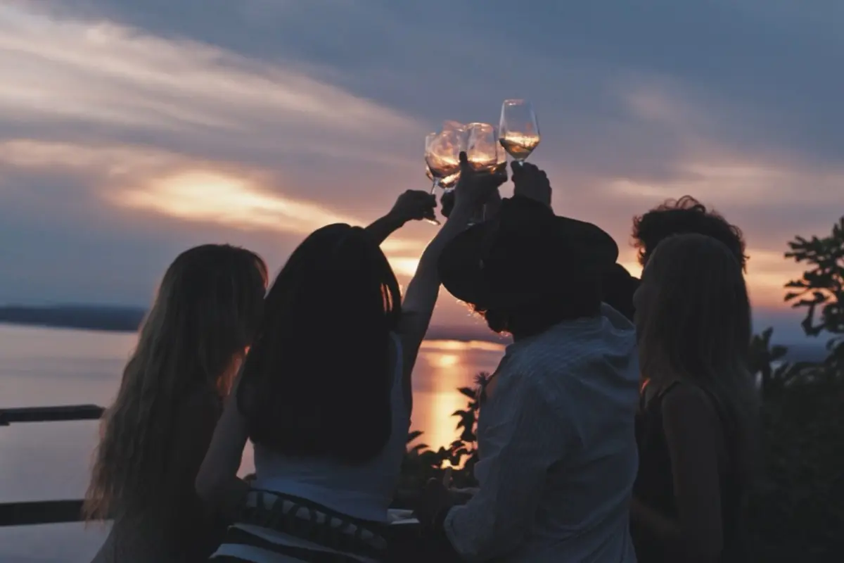 Grupo de amigos brindando con copas de vino al atardecer frente al mar