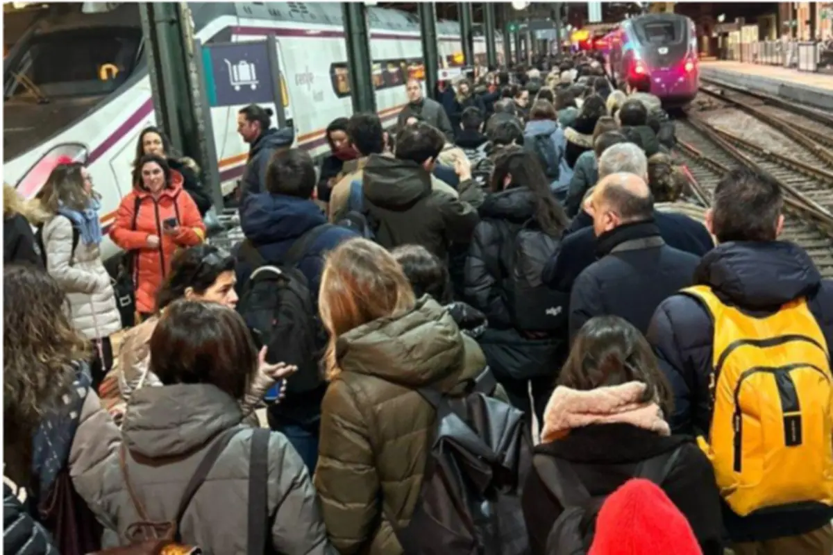Andén de estación de tren abarrotado de personas con abrigos y mochilas esperando junto a varios trenes detenidos