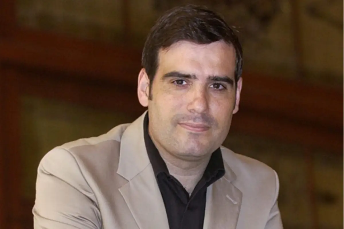 Retrato de un hombre de mediana edad con chaqueta beige y camisa negra mirando a la cámara con expresión seria y fondo interior desenfocado Retrato de un hombre de mediana edad con chaqueta beige y camisa negra mirando a la cámara con expresión seria y fondo interior desenfocado