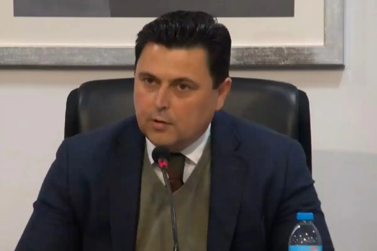 Hombre de mediana edad con traje hablando frente a un micrófono en una sala de conferencias