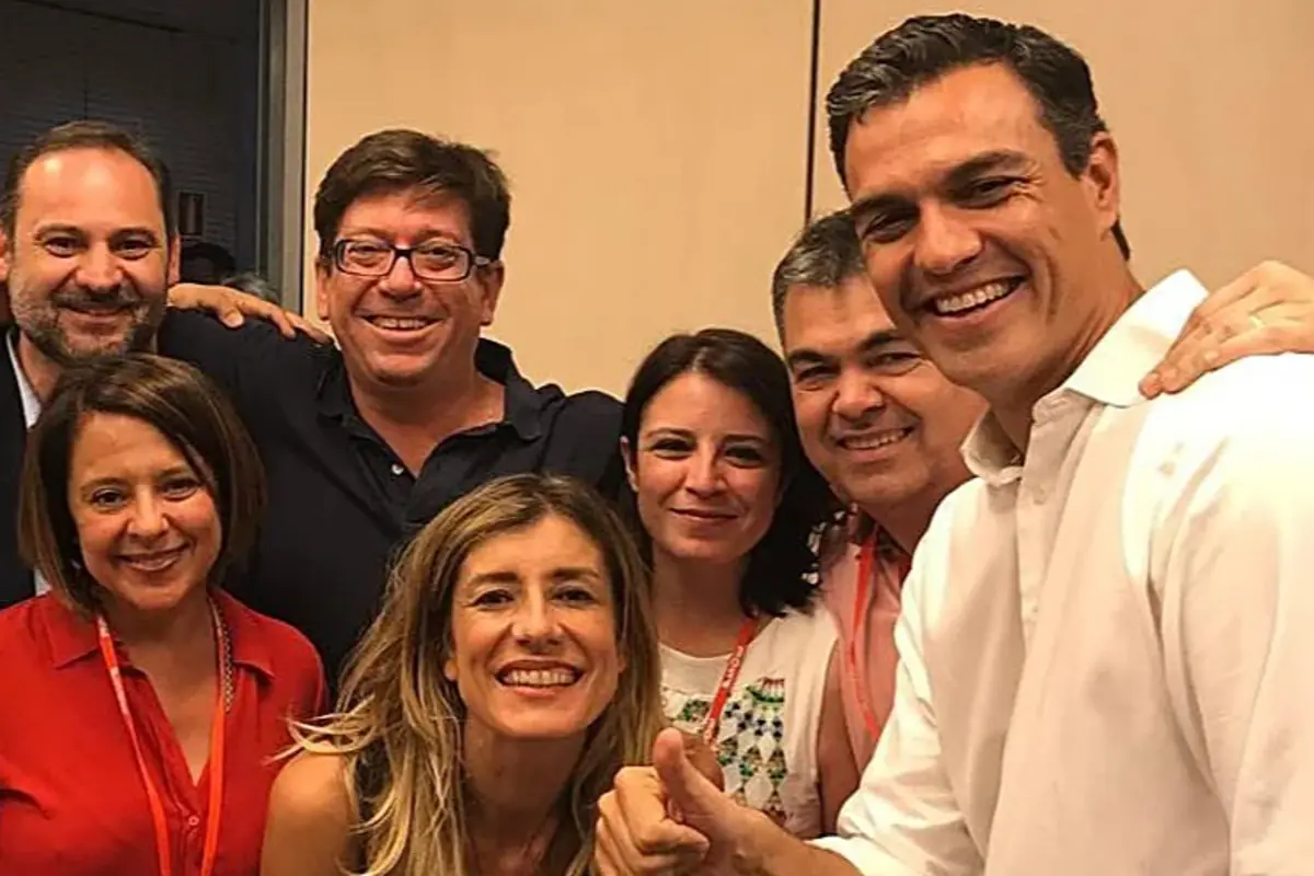 Grupo de siete personas adultas sonriendo y posando juntas en interior con actitud amistosa