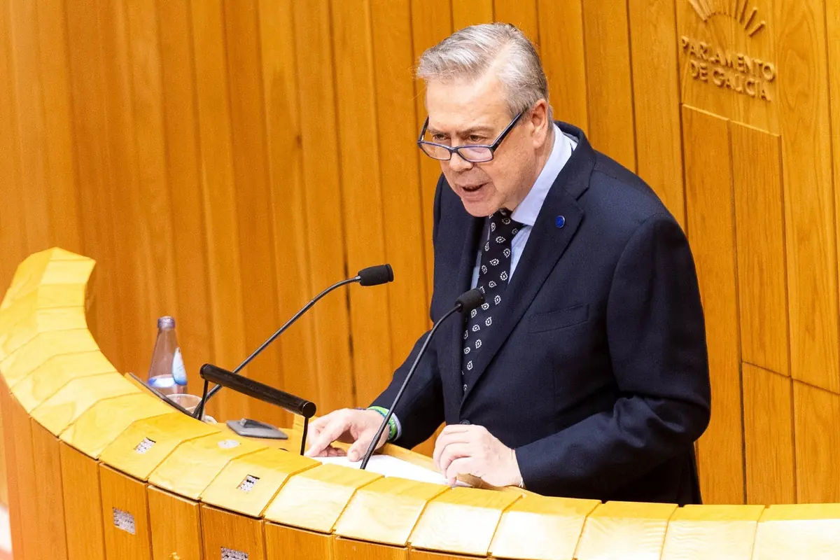 Hombre mayor con traje oscuro y gafas hablando en un atril de madera en el Parlamento de Galicia