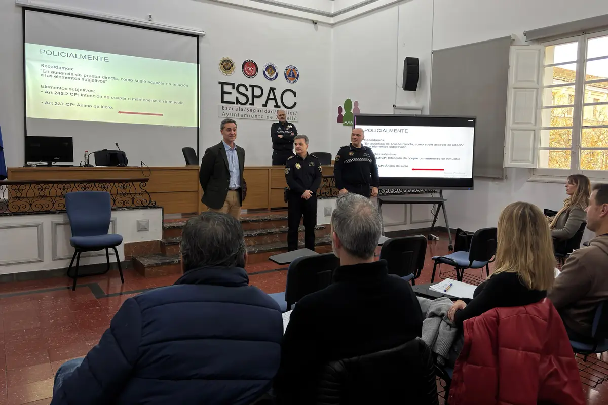 Personas asistentes a una charla formativa en un aula de la Escuela de Seguridad Pública de un ayuntamiento con varios agentes de policía exponiendo información proyectada en pantallas frente al público sentado