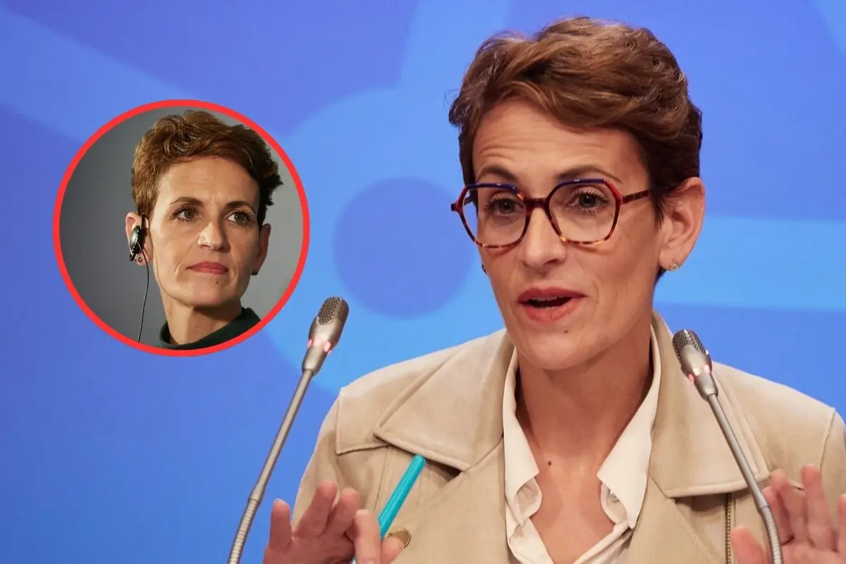 Mujer de pelo corto y gafas hablando en una rueda de prensa con micrófonos frente a ella y un recuadro circular que muestra otro retrato suyo con auricular en la oreja