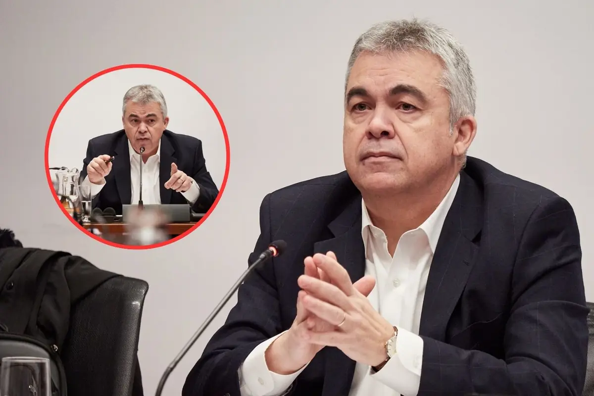 Hombre de mediana edad con traje oscuro y camisa blanca sentado frente a un micrófono en una reunión formal con un recuadro circular que muestra otra escena suya hablando y gesticulando en la misma sala