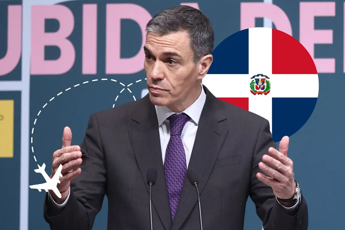 Hombre de traje hablando en un podio con micrófonos frente a un fondo gráfico que incluye un avión dibujado y la bandera de la República Dominicana