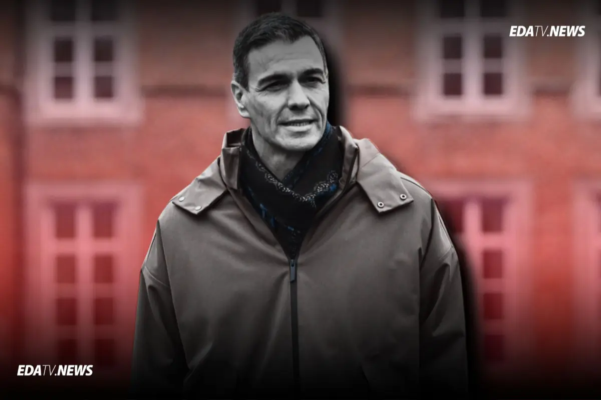 Hombre con abrigo oscuro y bufanda posando al aire libre frente a un edificio desenfocado con ventanas