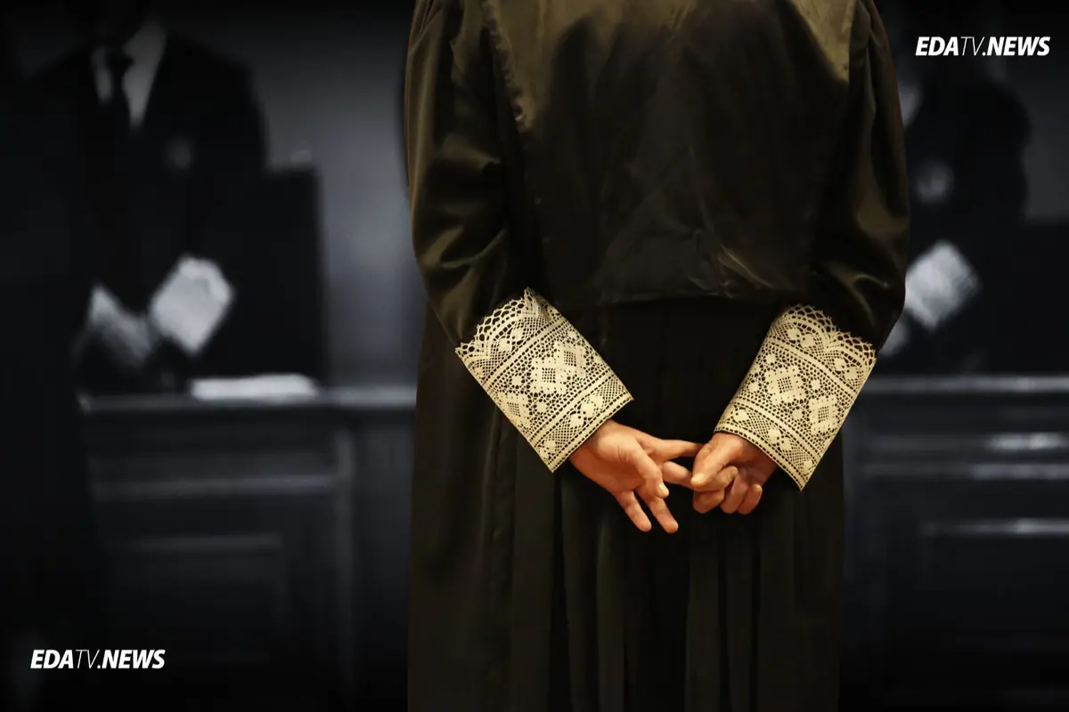 Juez de espaldas con toga negra y puños de encaje entrelazando las manos en una sala de tribunal