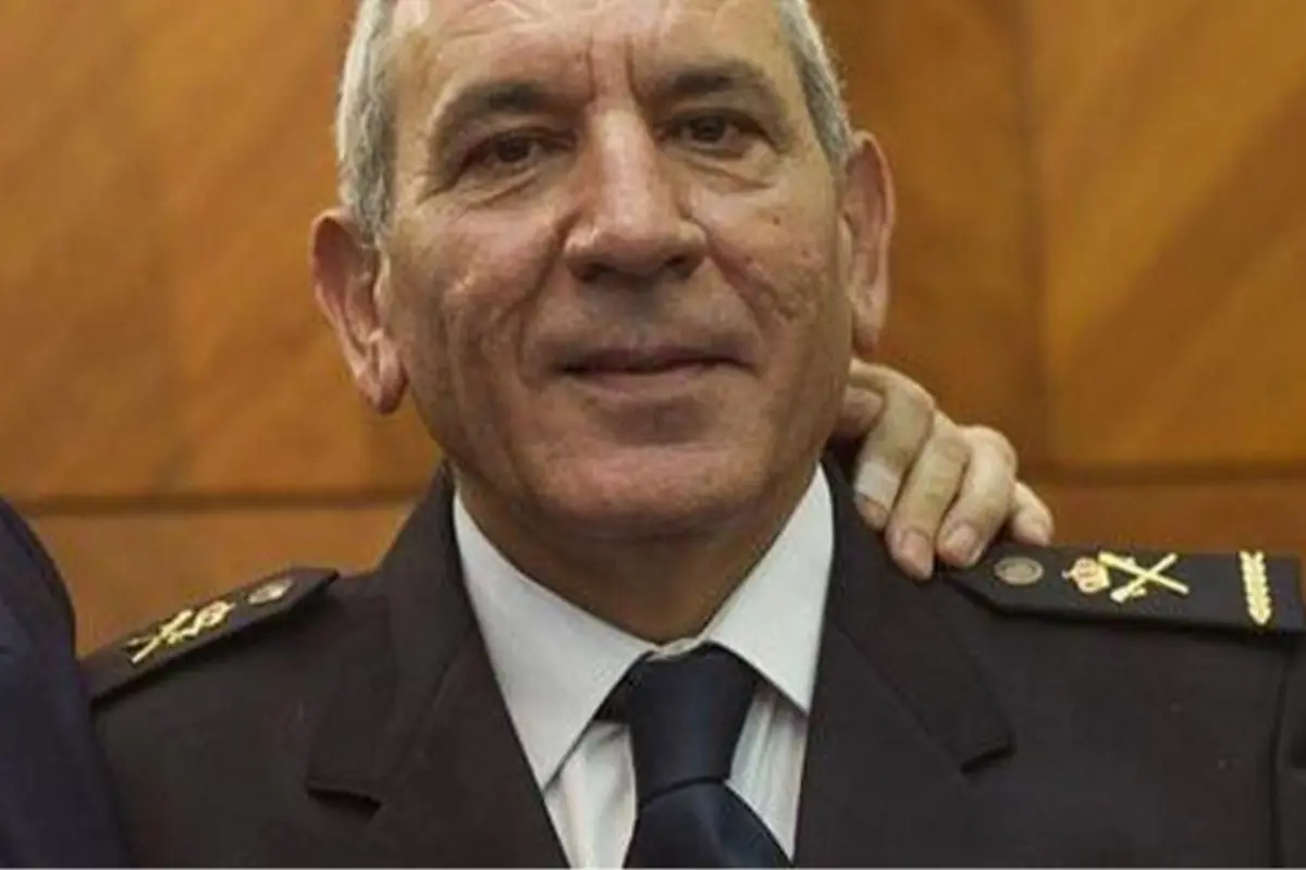 Hombre de mediana edad con uniforme militar oscuro y corbata, posando en interior con una mano apoyada en su hombro