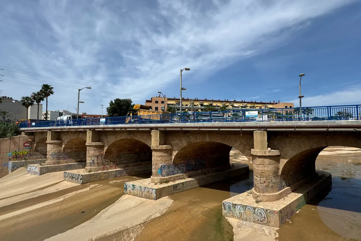 Puente de piedra con varios arcos sobre un cauce casi seco con grafitis en los pilares y barandillas azules bajo un cielo parcialmente nublado Puente de piedra con varios arcos sobre un cauce casi seco con grafitis en los pilares y barandillas azules bajo un cielo parcialmente nublado