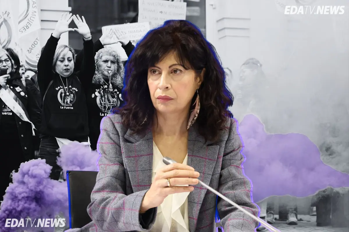 Mujer de mediana edad hablando al micrófono en un acto público con fondo de manifestación feminista y humo morado
