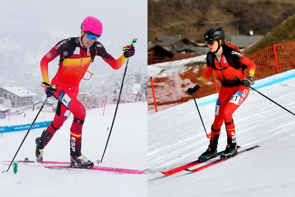 Dos esquiadores de travesía con mono rojo de España compiten en la nieve usando bastones y casco en una pista delimitada por vallas naranjas