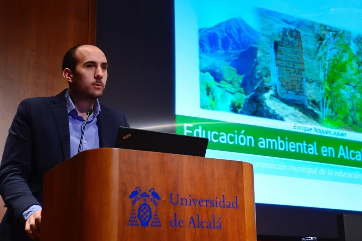 Hombre dando una conferencia sobre educación ambiental en un auditorio de la Universidad de Alcalá con una presentación proyectada al fondo