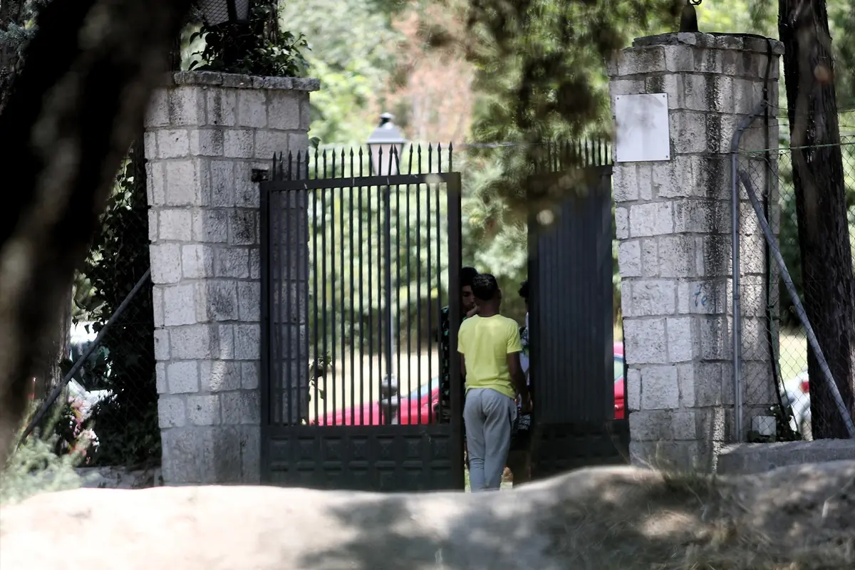 Niños conversando junto a un portón metálico abierto entre dos pilares de piedra en un entorno arbolado