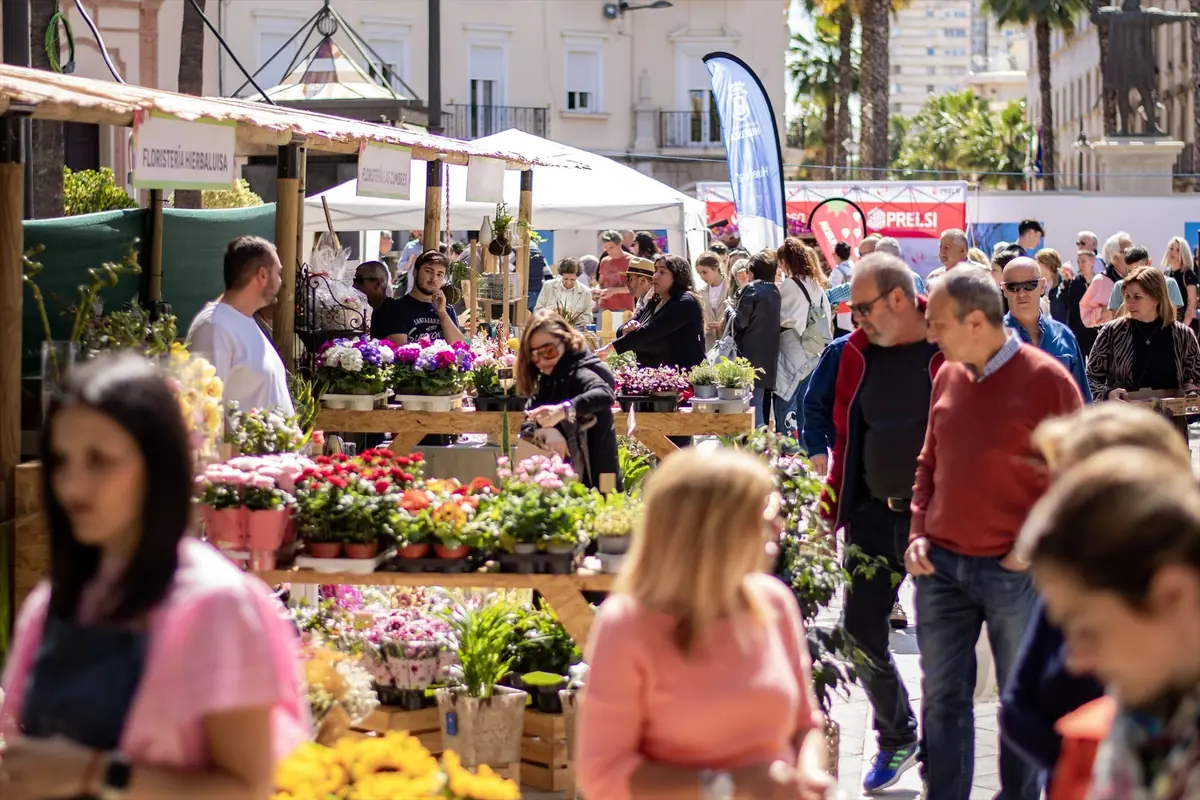 Personas pasean y compran plantas y flores en un mercado al aire libre lleno de puestos de madera en un día soleado