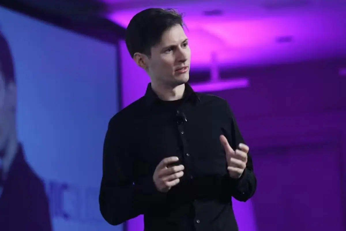 Hombre joven con camisa negra dando una conferencia en un escenario iluminado con luces moradas