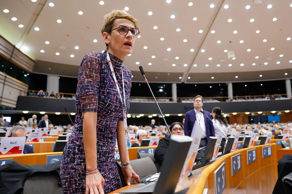 Mujer de pie hablando frente a un micrófono en un gran auditorio lleno de delegados y pantallas de votación
