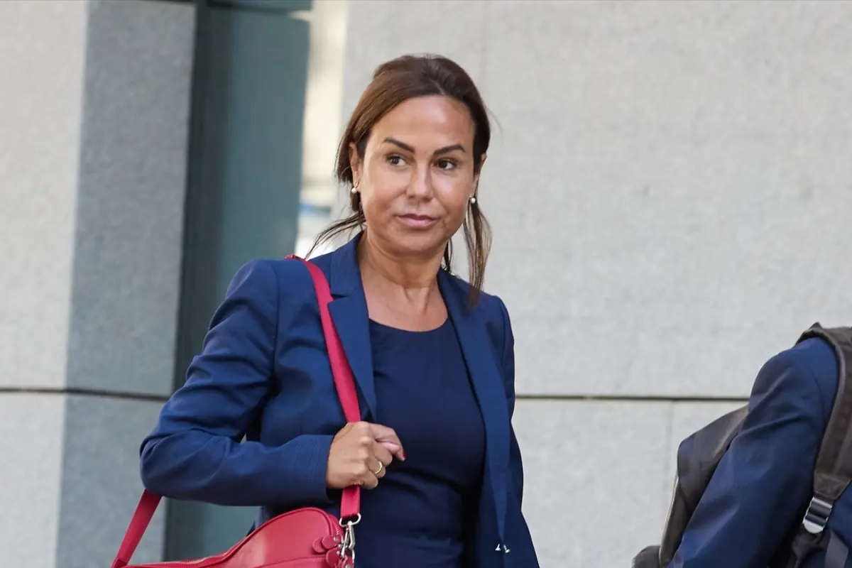 Mujer con traje azul marino caminando junto a un edificio de piedra y llevando un bolso rojo sobre el hombro