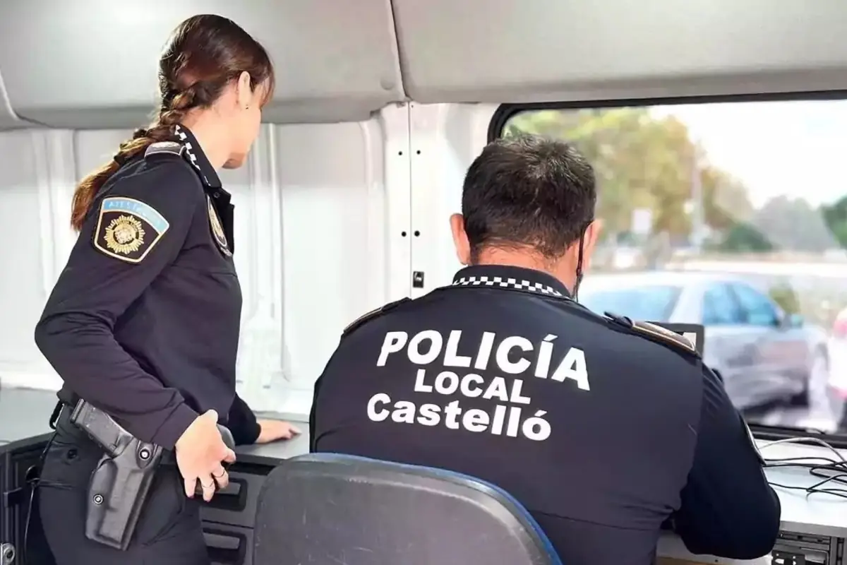 Dos agentes de la Policía Local de Castelló trabajando dentro de un vehículo policial frente a una ventana con vista a la calle
