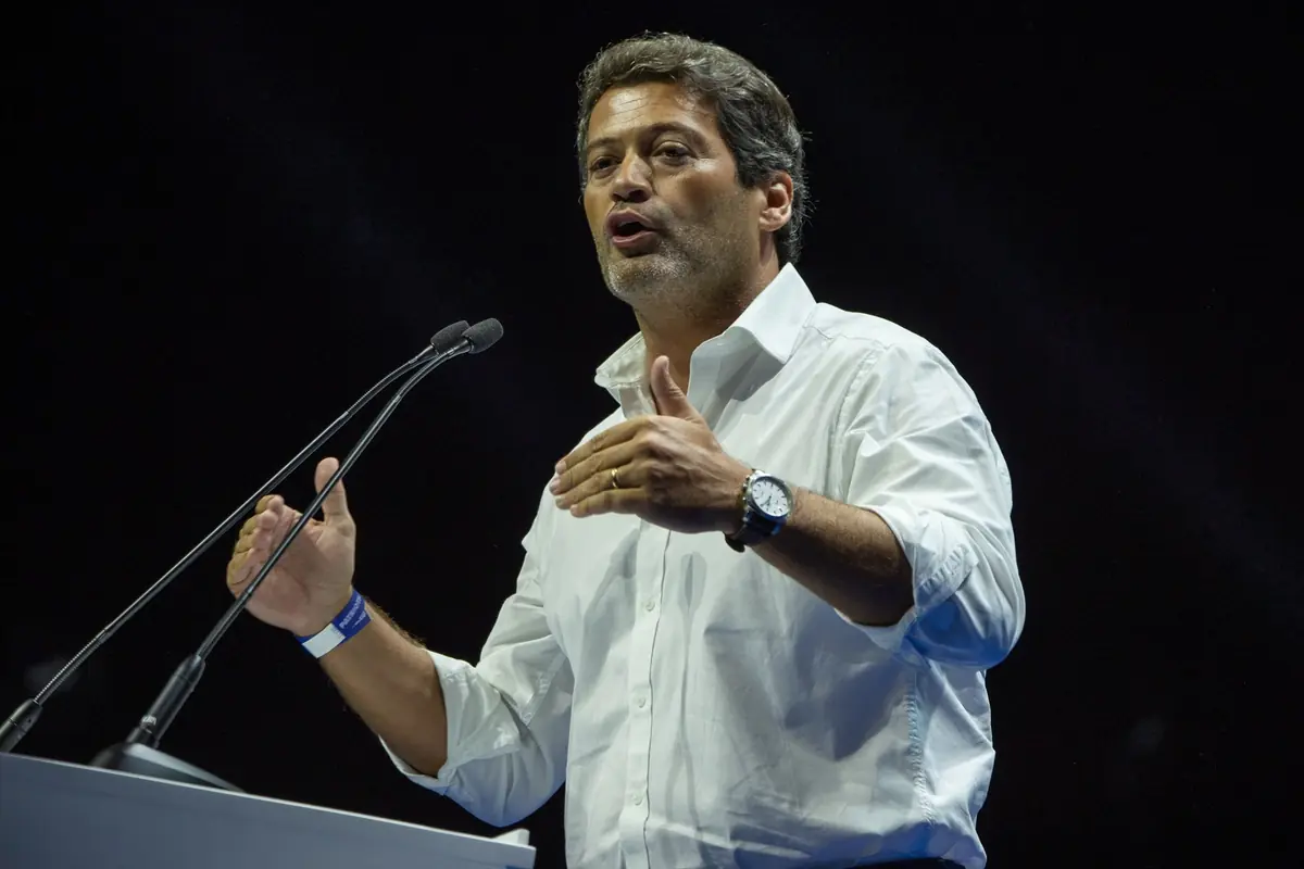 Hombre con camisa blanca hablando apasionadamente frente a dos micrófonos en un escenario oscuro Hombre con camisa blanca hablando apasionadamente frente a dos micrófonos en un escenario oscuro