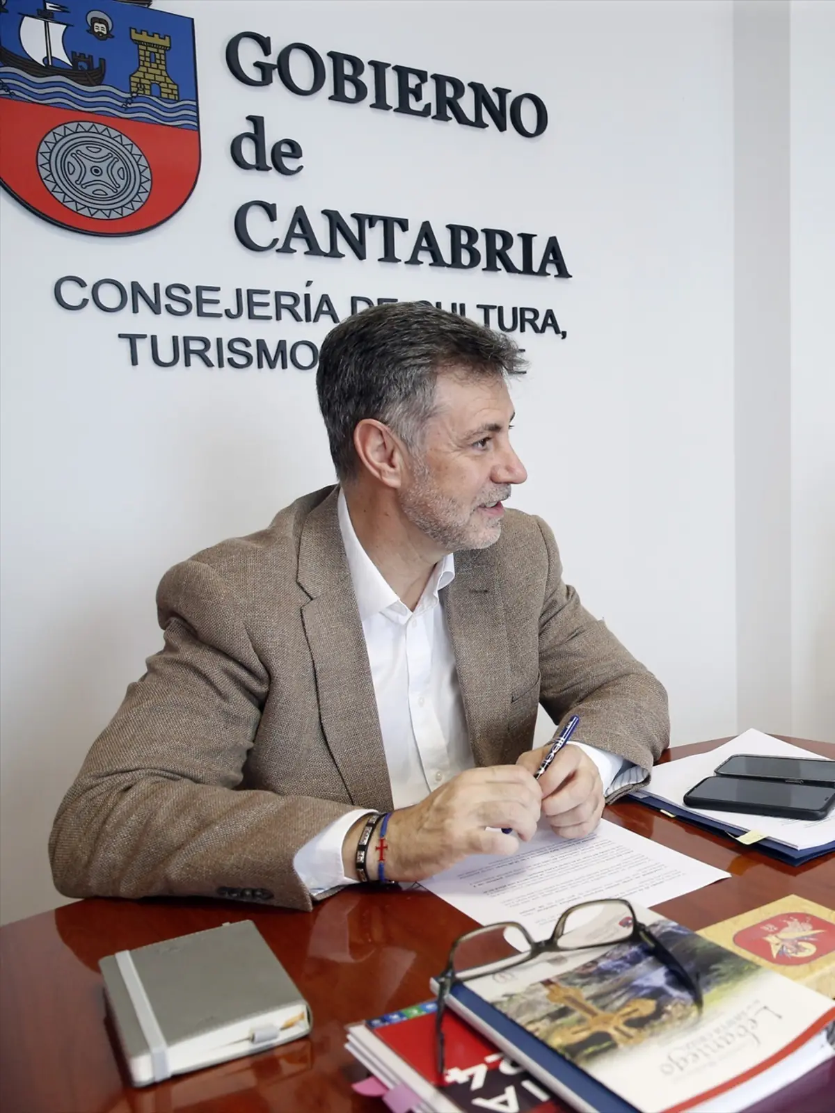 Hombre de mediana edad con chaqueta beige trabajando en una mesa de despacho en la Consejería de Cultura y Turismo del Gobierno de Cantabria