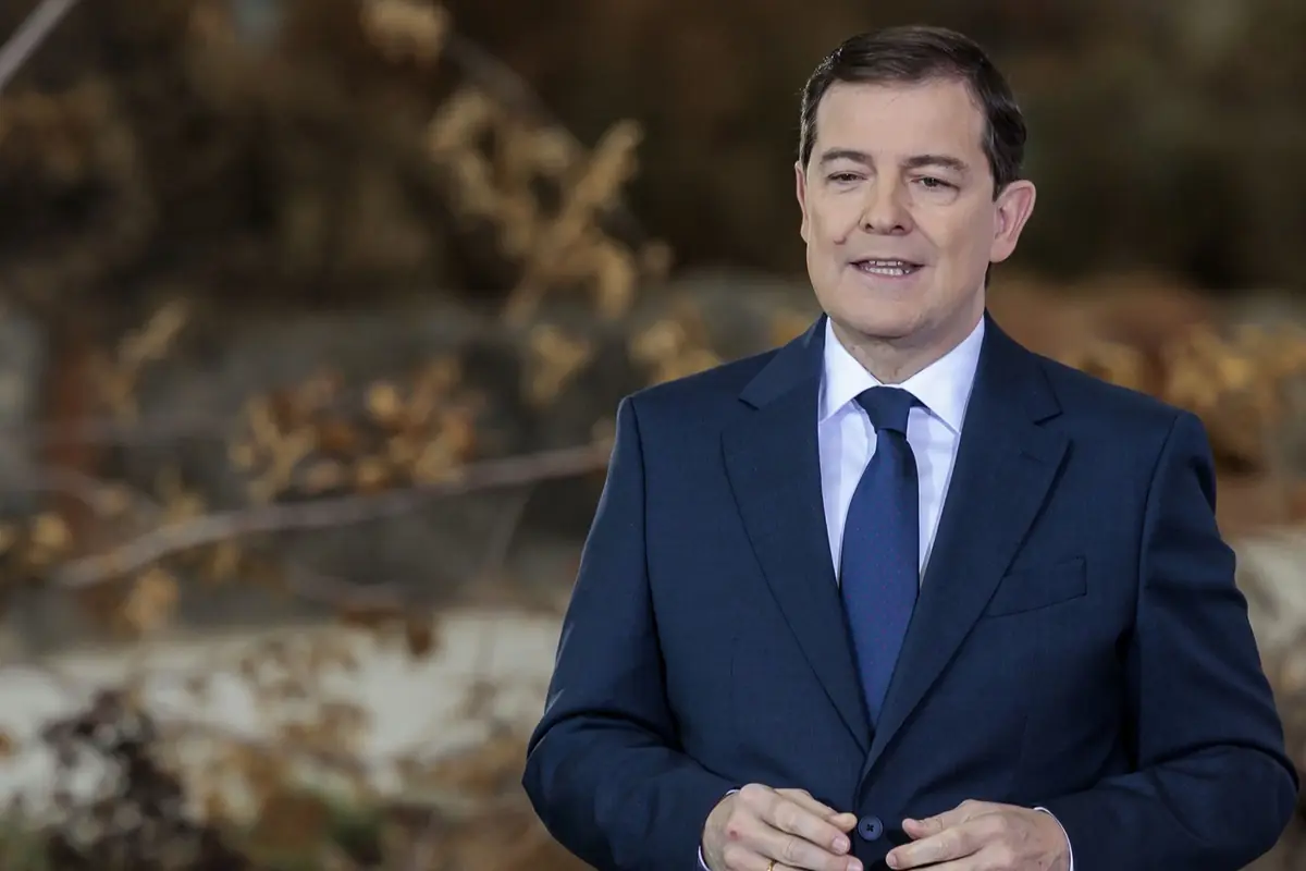 Hombre con traje azul oscuro y corbata hablando frente a un fondo desenfocado de tonos marrones
