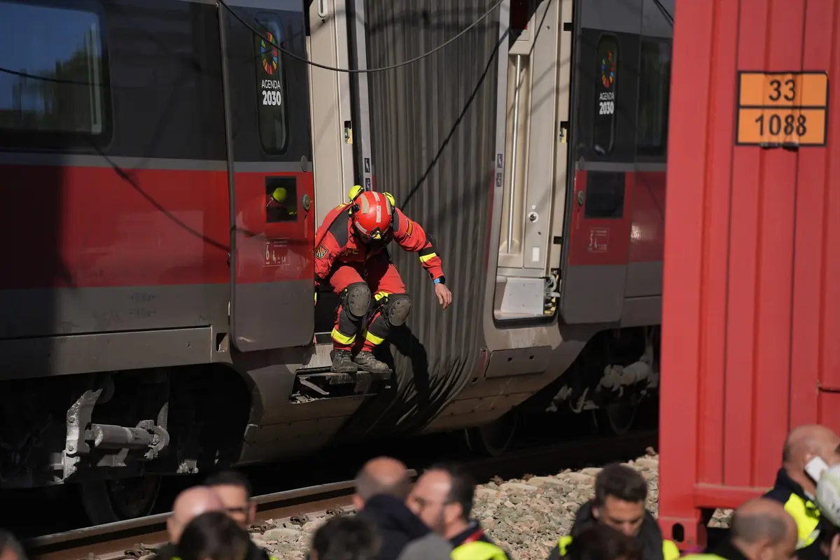 Rescatista con casco y uniforme rojo desciende de un tren detenido en las vías mientras varias personas observan la escena desde el suelo