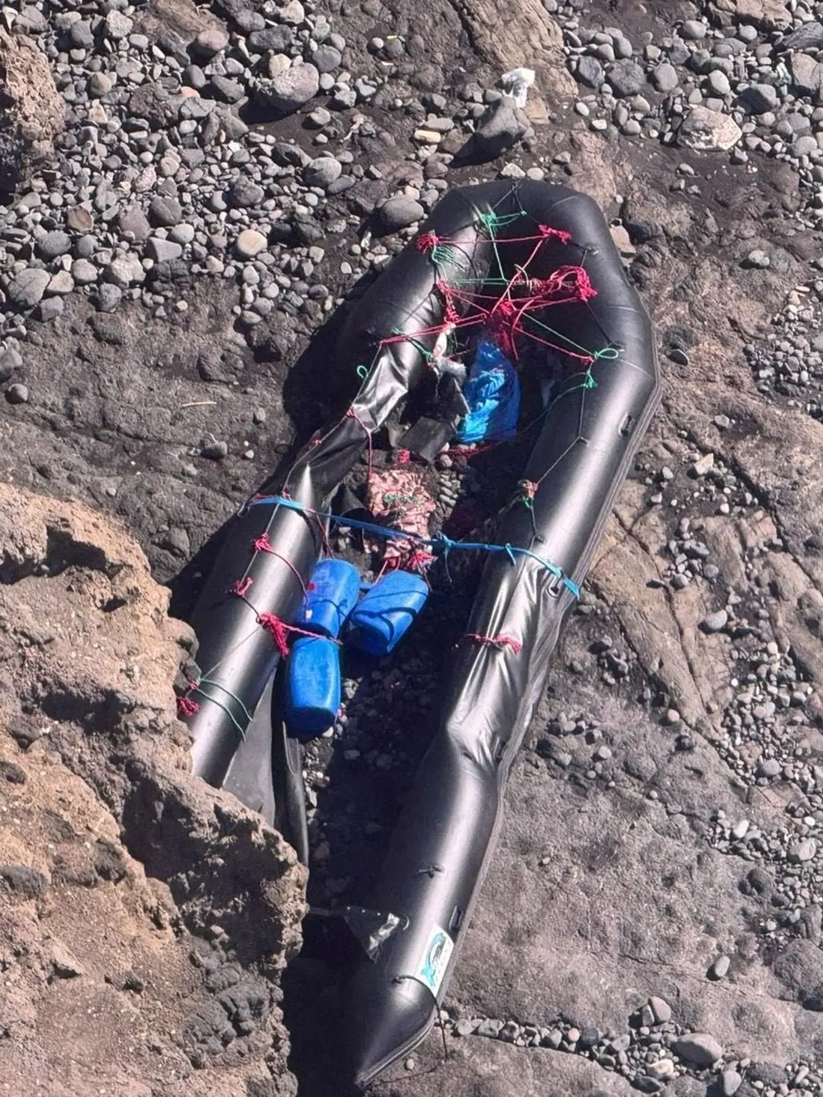 Balsa neumática negra dañada y abandonada entre rocas en una playa de piedras