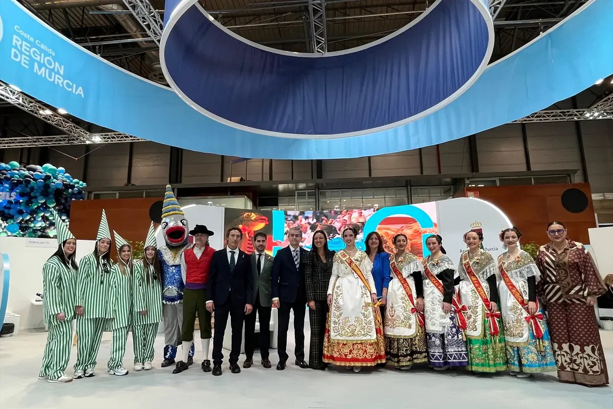Grupo de personas con trajes tradicionales y disfraces festivos posando en un stand promocional de la Región de Murcia en una feria turística